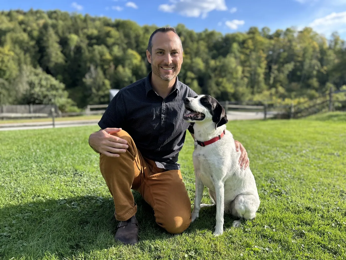 Patrick Cassidy kneeling in a grassy Vermont field beside his dog