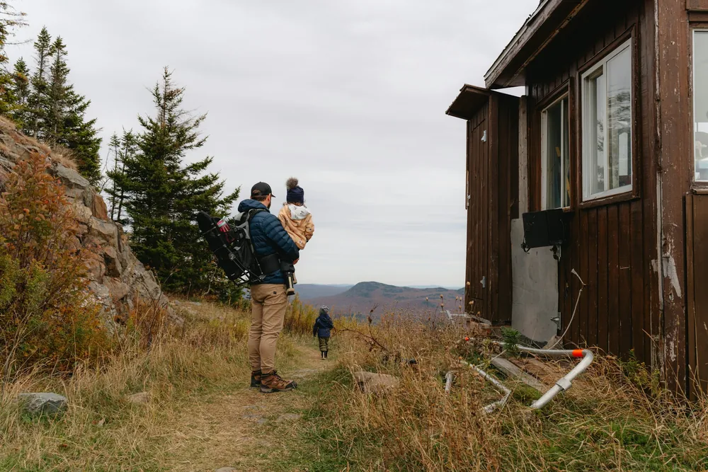 A father carrying his child on a trail near a cabin
