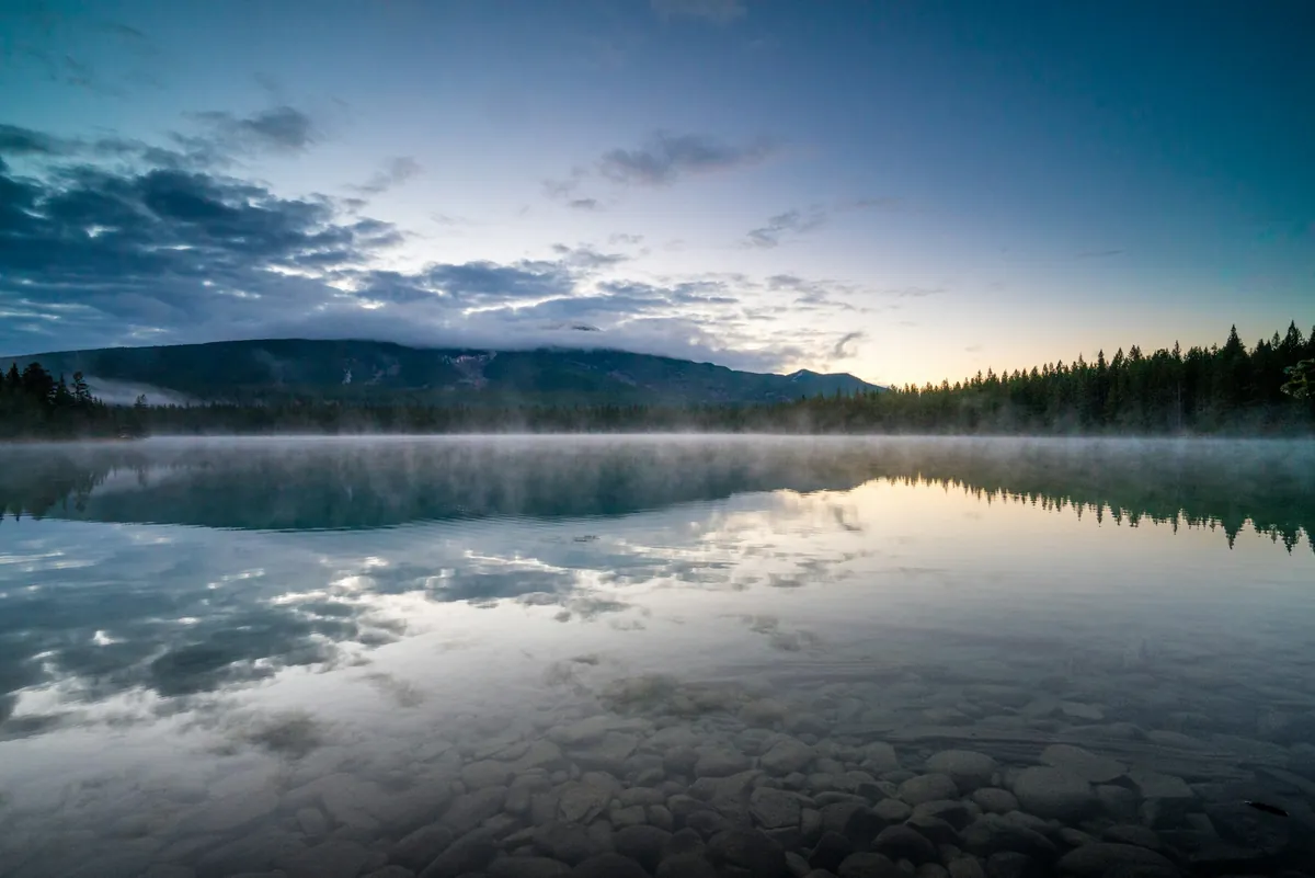 A still Vermont lake at dawn, mist rising off the water